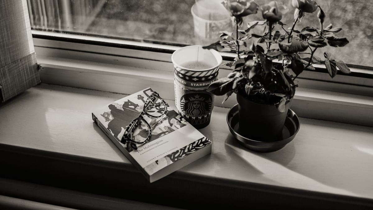 A coffee cup beside an open book on a windowsill