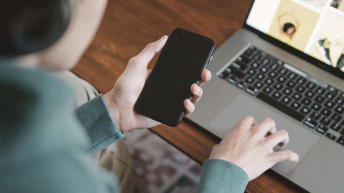 A person using a smartphone beside a laptop at a desk