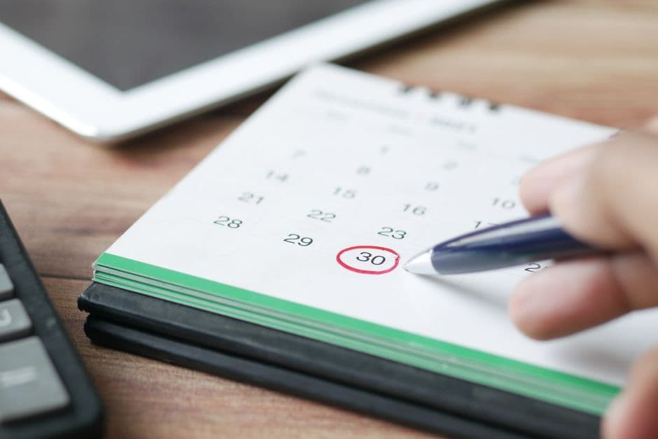 A hand marking a date on a wall calendar