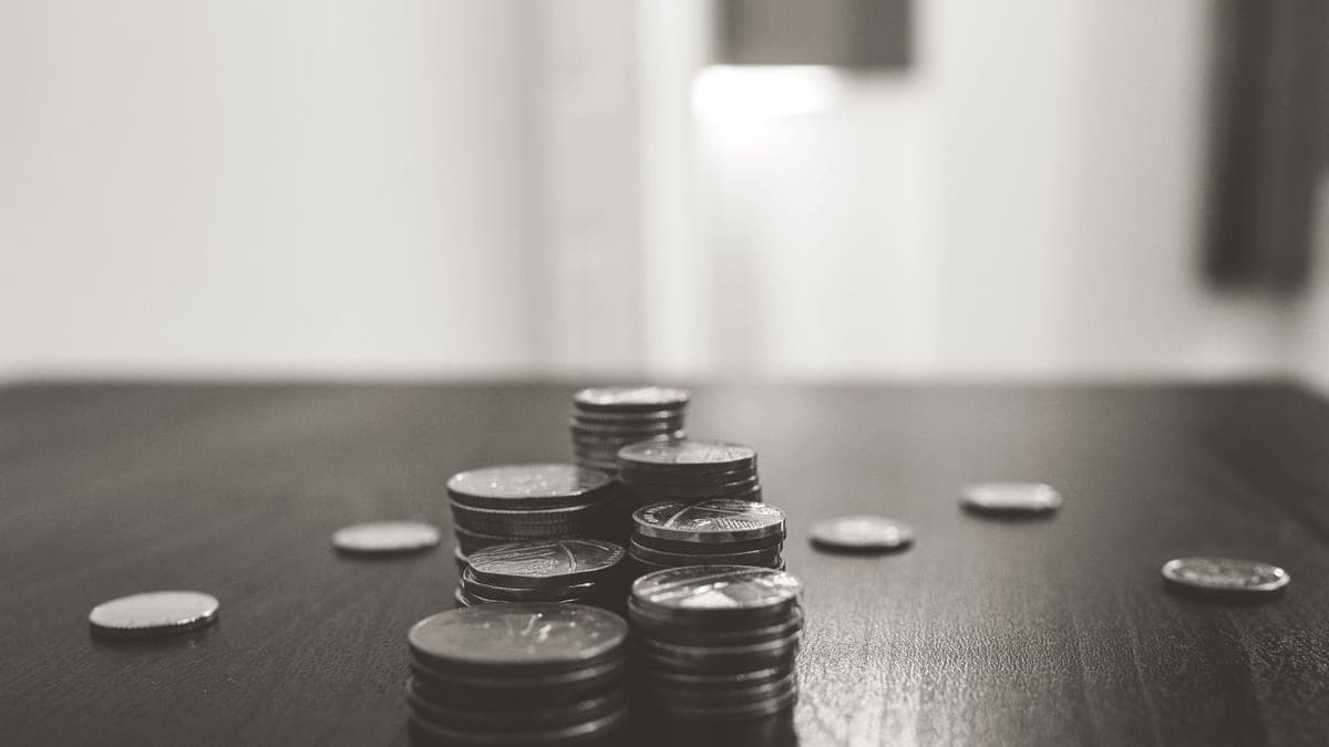 A small stack of coins beside a book on a wooden table