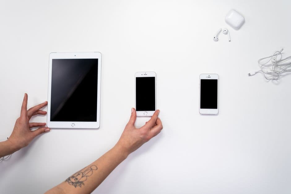 A tablet, two phones and earphones arranged on a white surface