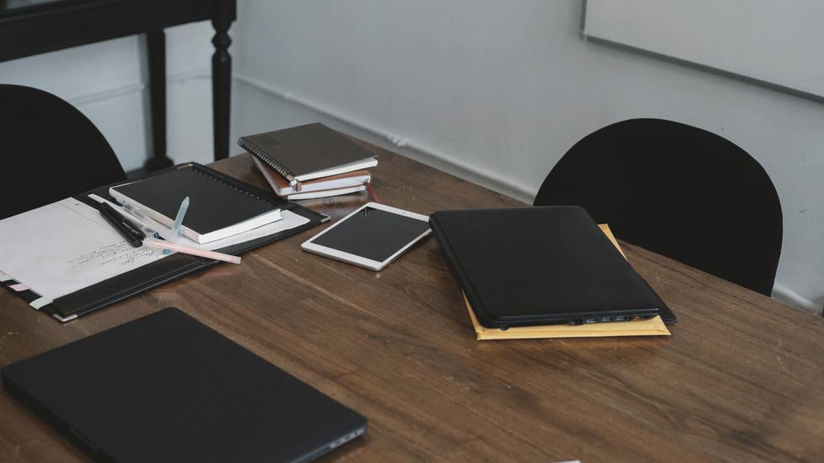 A laptop and tablet on a wooden desk with notebooks