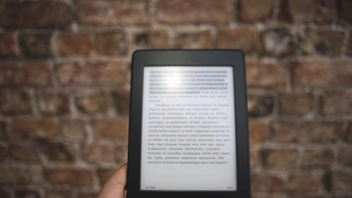 A hand holding an e-reader in front of a brick wall