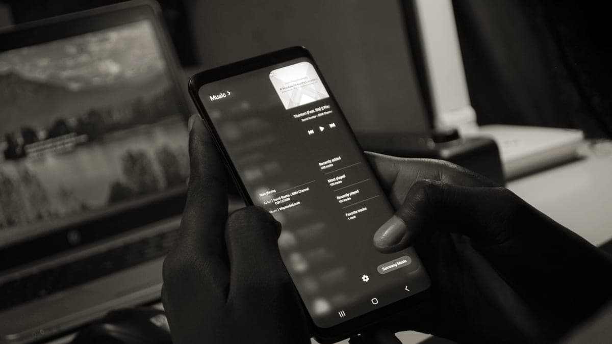 A hand holding a smartphone showing an audio player, with headphones nearby
