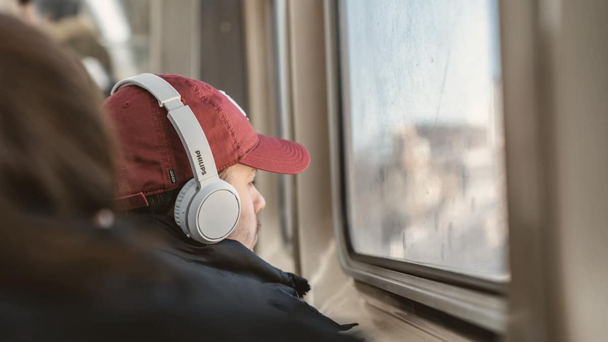 A man wearing headphones on a train, looking out of the window
