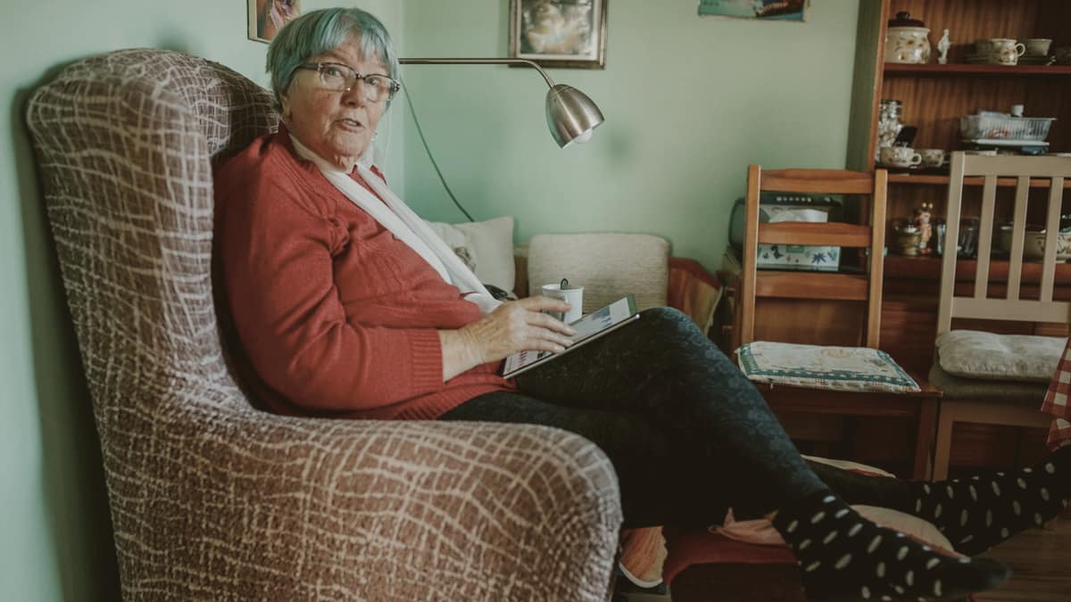 An older woman sitting comfortably at home, reading on a tablet