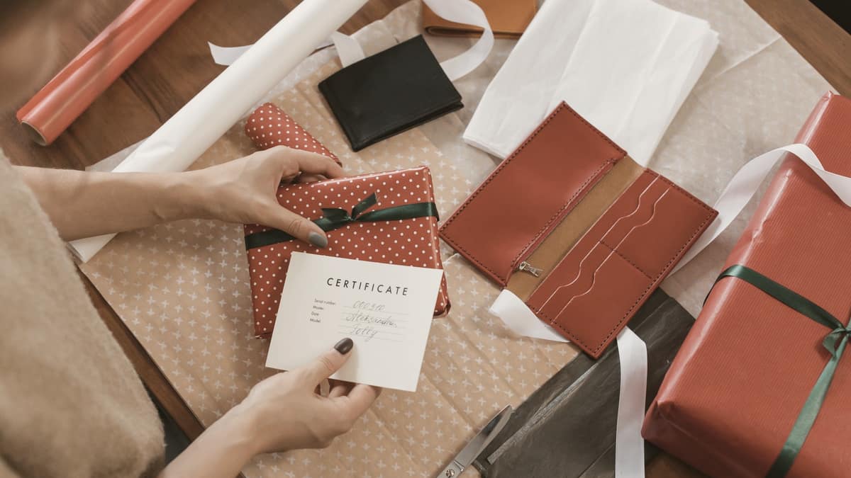 Hands wrapping a present with a gift certificate on a wooden table