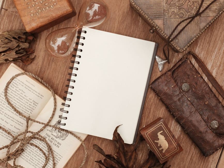 An open notebook, a book and an hourglass on a wooden surface