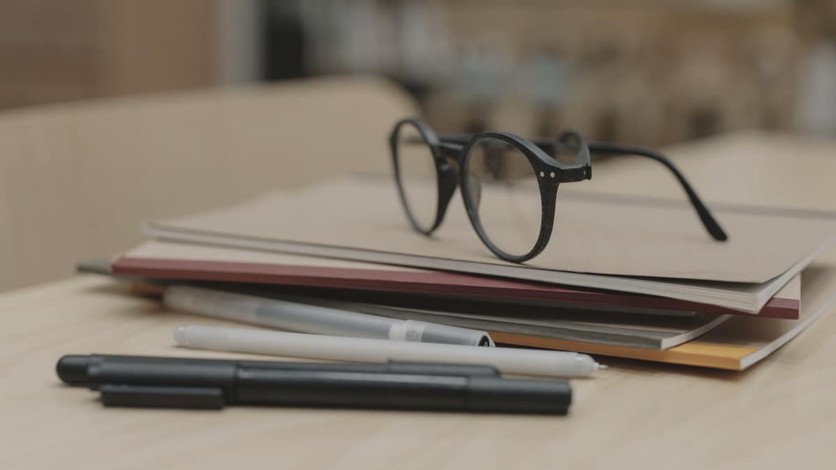 Reading glasses resting on a stack of notebooks with pens