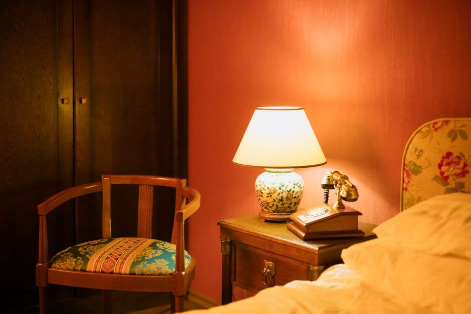 A warm bedside lamp beside a chair in a dim bedroom