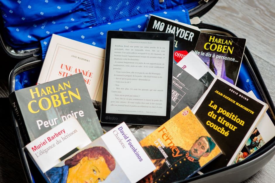 Paperback books and an e-reader packed together in an open suitcase