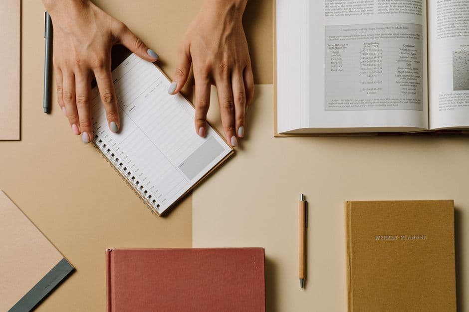 Hands arranging books and planners on a desk, seen from above