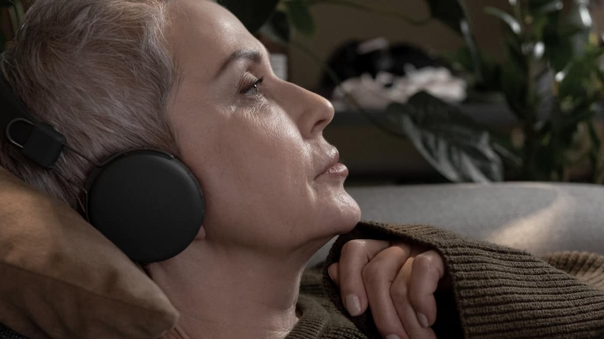 An older woman sitting in an armchair wearing headphones