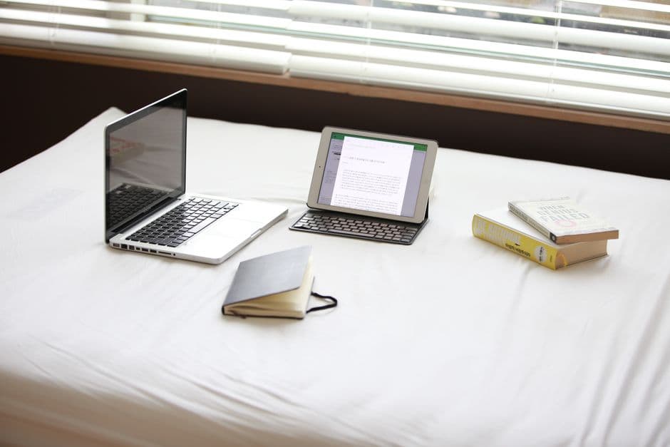 A tablet, notebook and books laid out on a bed