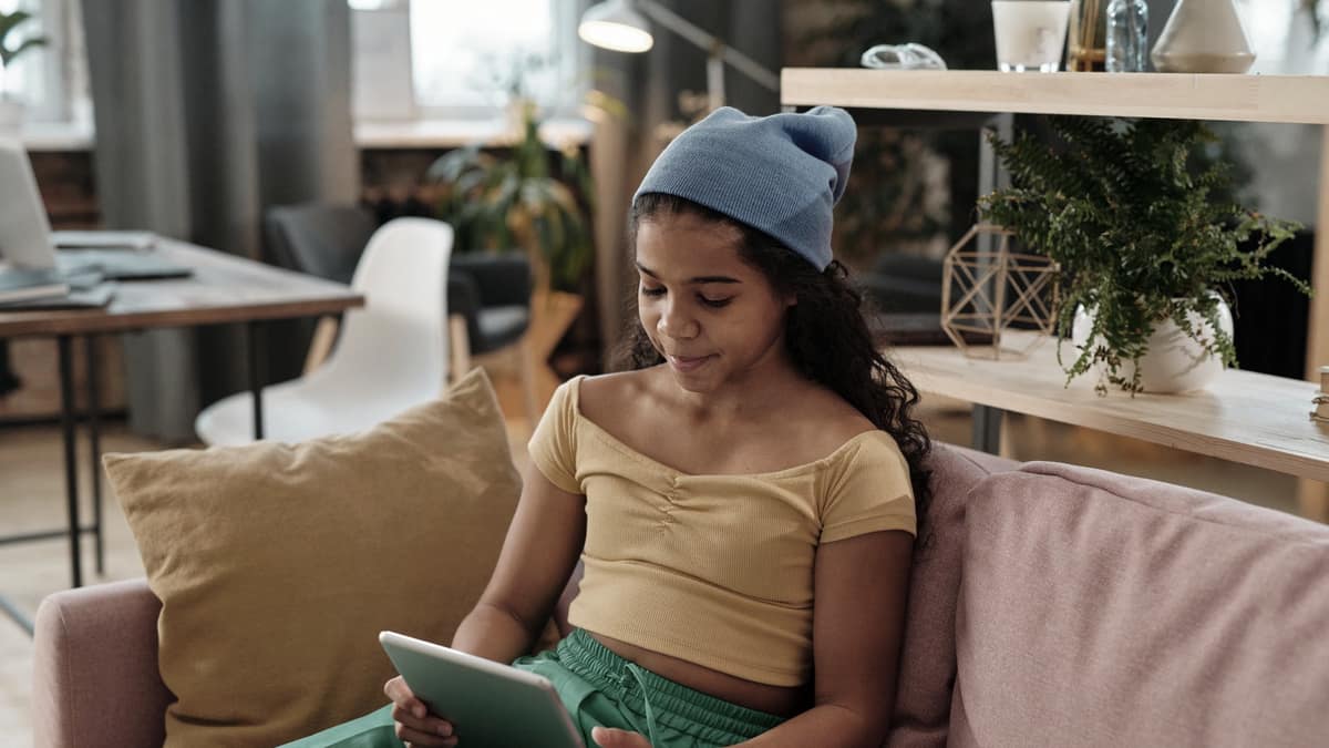 A teenager reading on a tablet on a sofa