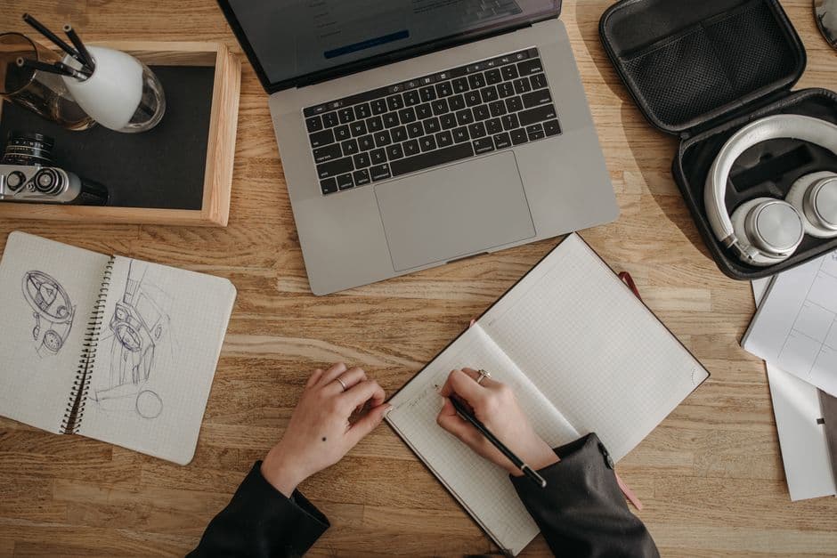 A laptop, sketchbooks and headphones on a wooden desk, seen from above