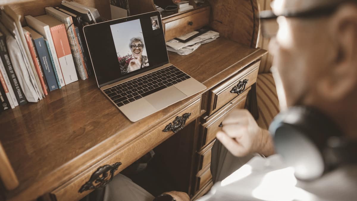 A man at a wooden desk with a laptop and headphones beside him